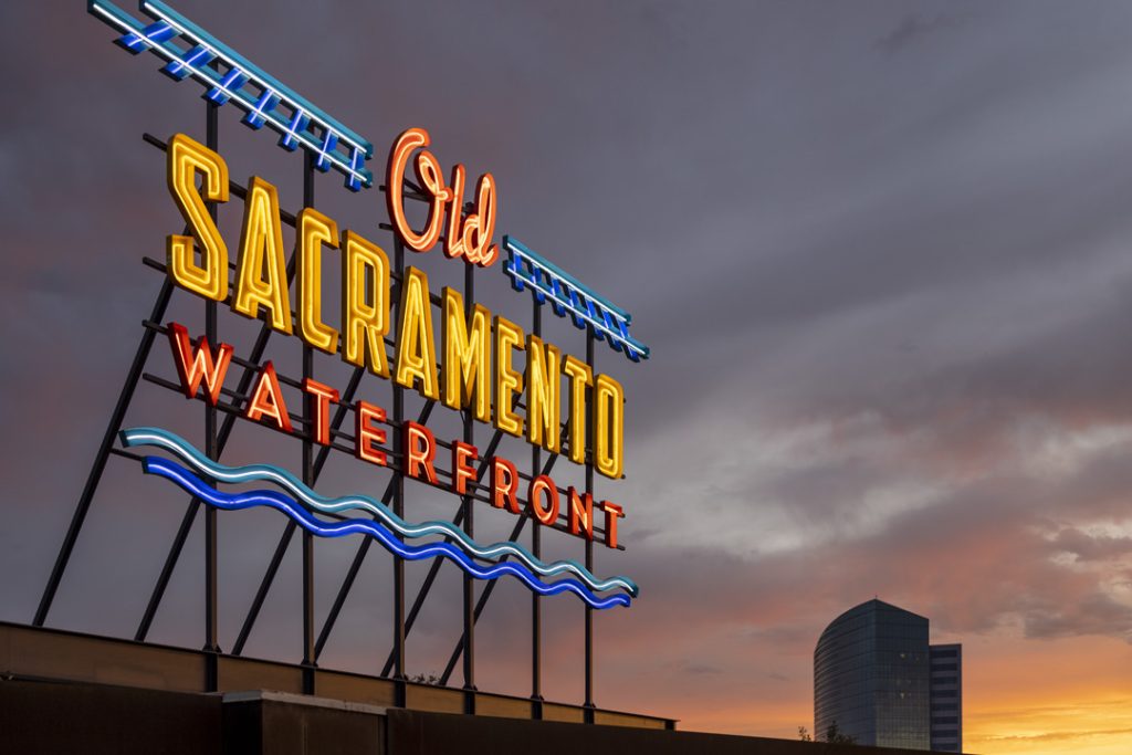 Neon Sign, "Old Sacramento Waterfront" at dusk with orange cloudy sky in the background.
