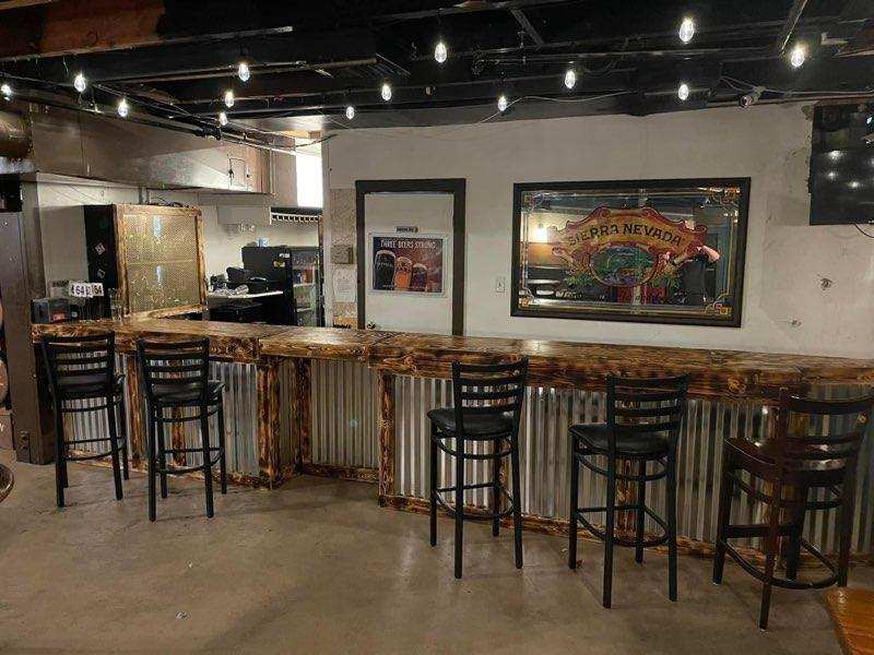 Long rustic wood bar with corrugated metal siding and black barstools under string lights at O’Mally’s Irish Pub