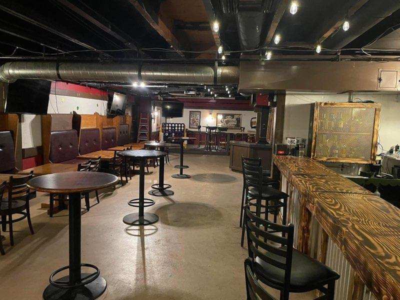 Dining room at O’Mally’s with tall bistro tables, tufted booth seating along the wall, and the wood bar on the right