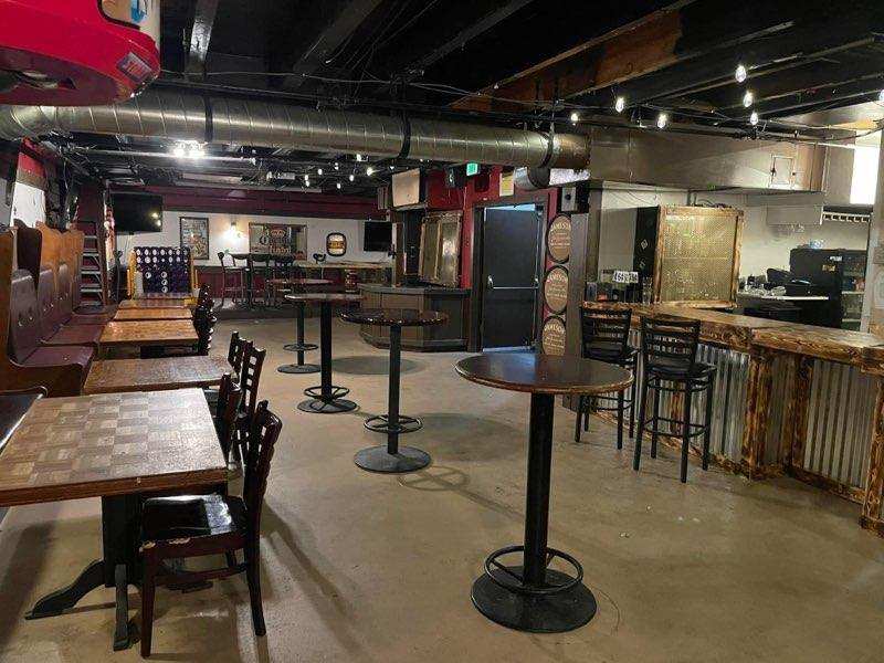 Wide view of O’Mally’s with booths, high-top tables, exposed ductwork, and the bar along the right wall