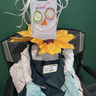 EcoPress Sacramento scarecrow with a face made from recycled materials and a sunflower collar