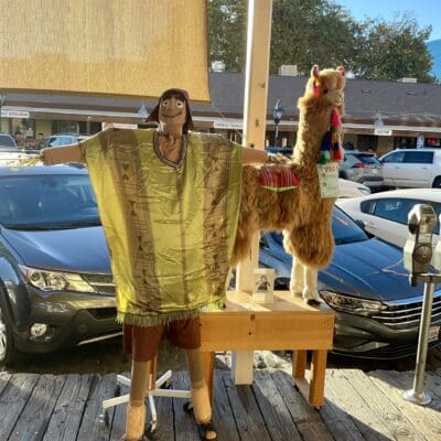 Peruvian Crafts scarecrow in a woven poncho beside an alpaca figure on the boardwalk