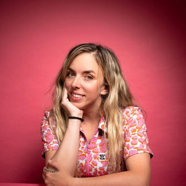 Comedian Jessica Michelle Singleton smiling with her hand on her chin against a pink background