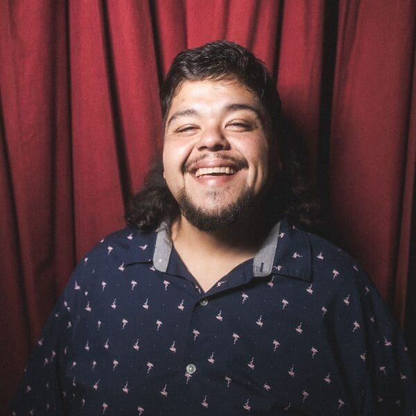 Comedian Saul Trujillo laughing in front of a red curtain