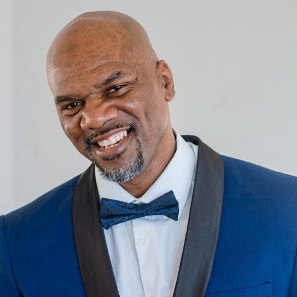 Comedian Mario Hodge grinning in a blue tuxedo jacket and bow tie