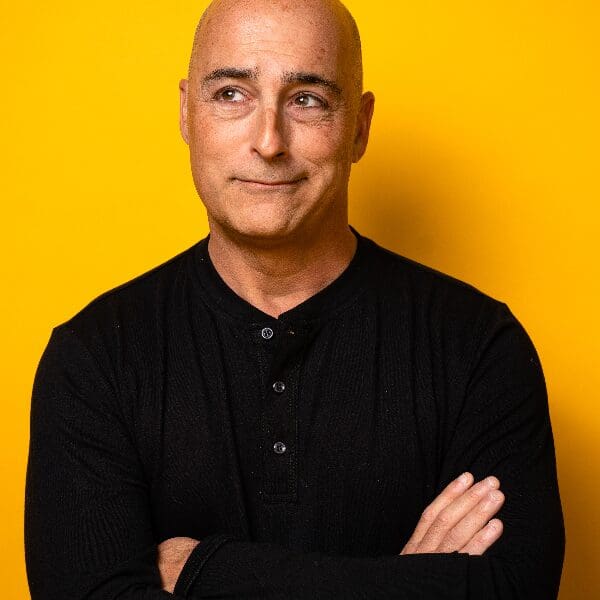 Comedian Cash Levy with arms crossed against a yellow background