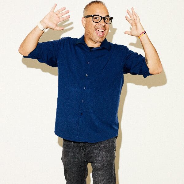 Comedian Manny Maldonado in glasses with his hands raised, laughing