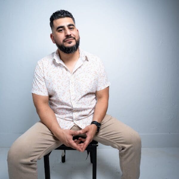 data-27 Comedian Rudy Ortiz seated on a stool in a white shirt against a light background